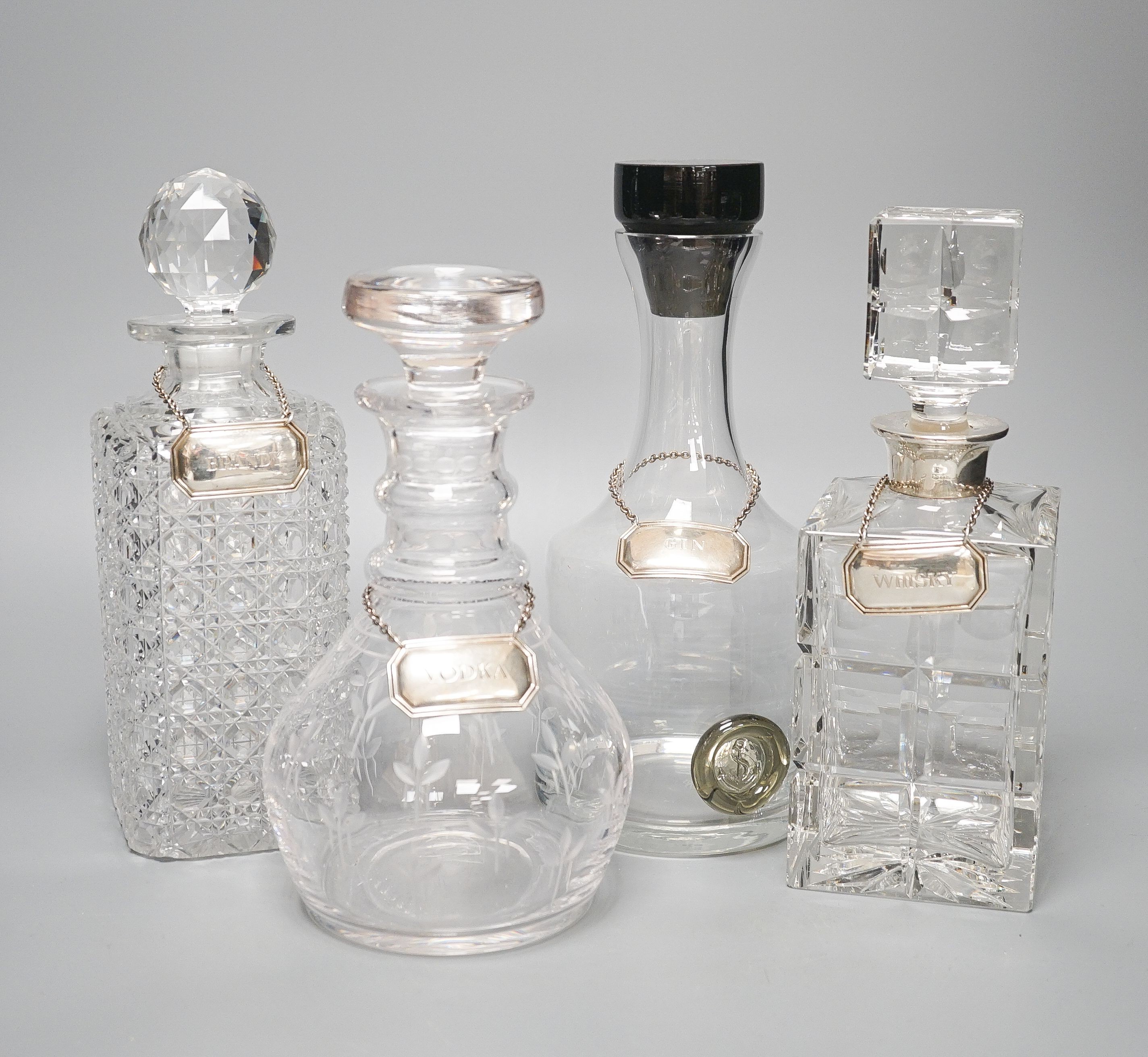 Four various glass decanters and silver labels for gin, brandy, vodka and whisky.